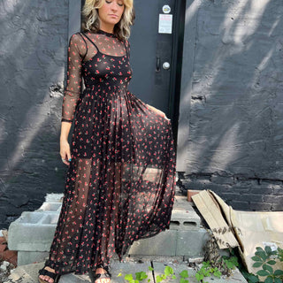 Woman holding out the hem of her cherry mesh maxi dress while standing on concrete steps.