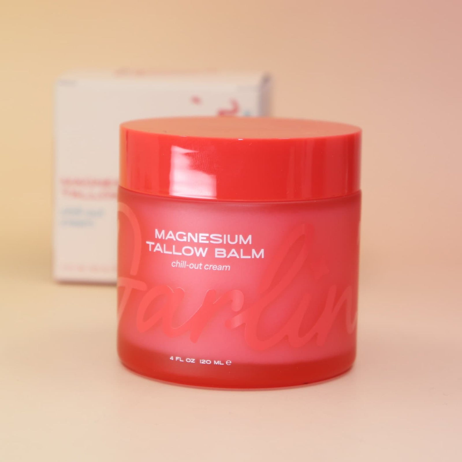 Red jar of magnesium tallow balm on a beige background