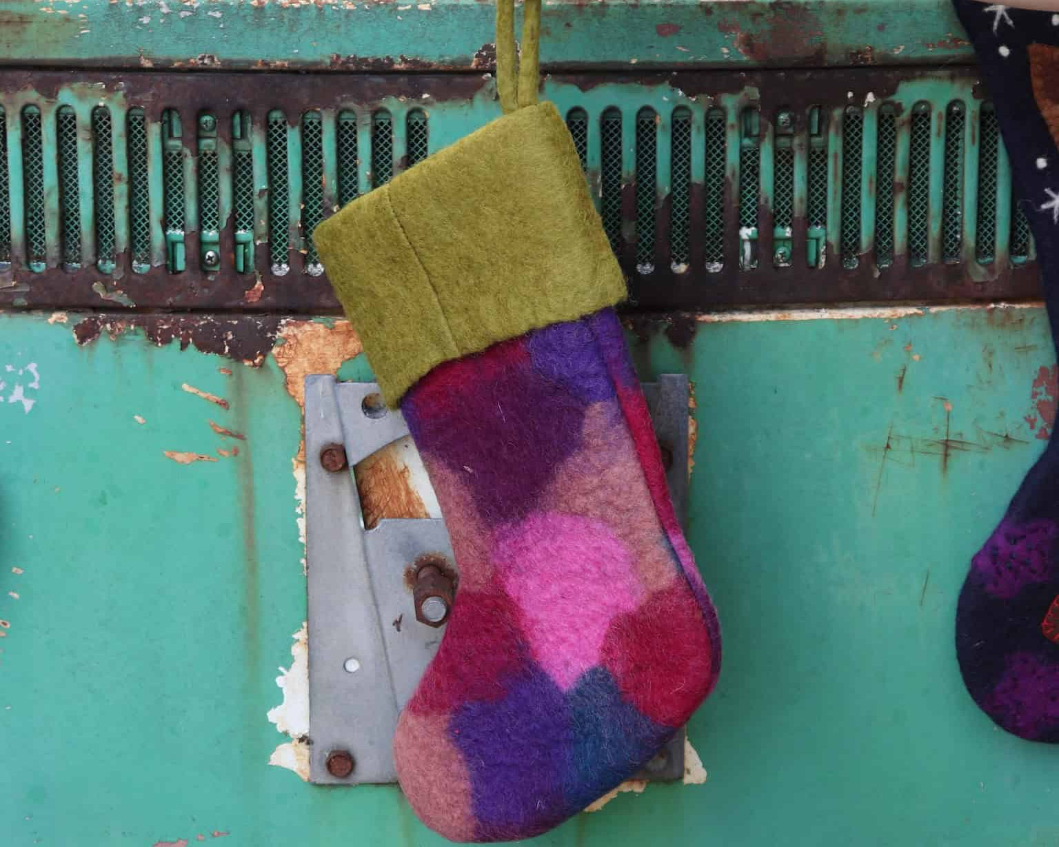 Colorful patterned christmas stocking being held by a hand against a rusty metal background