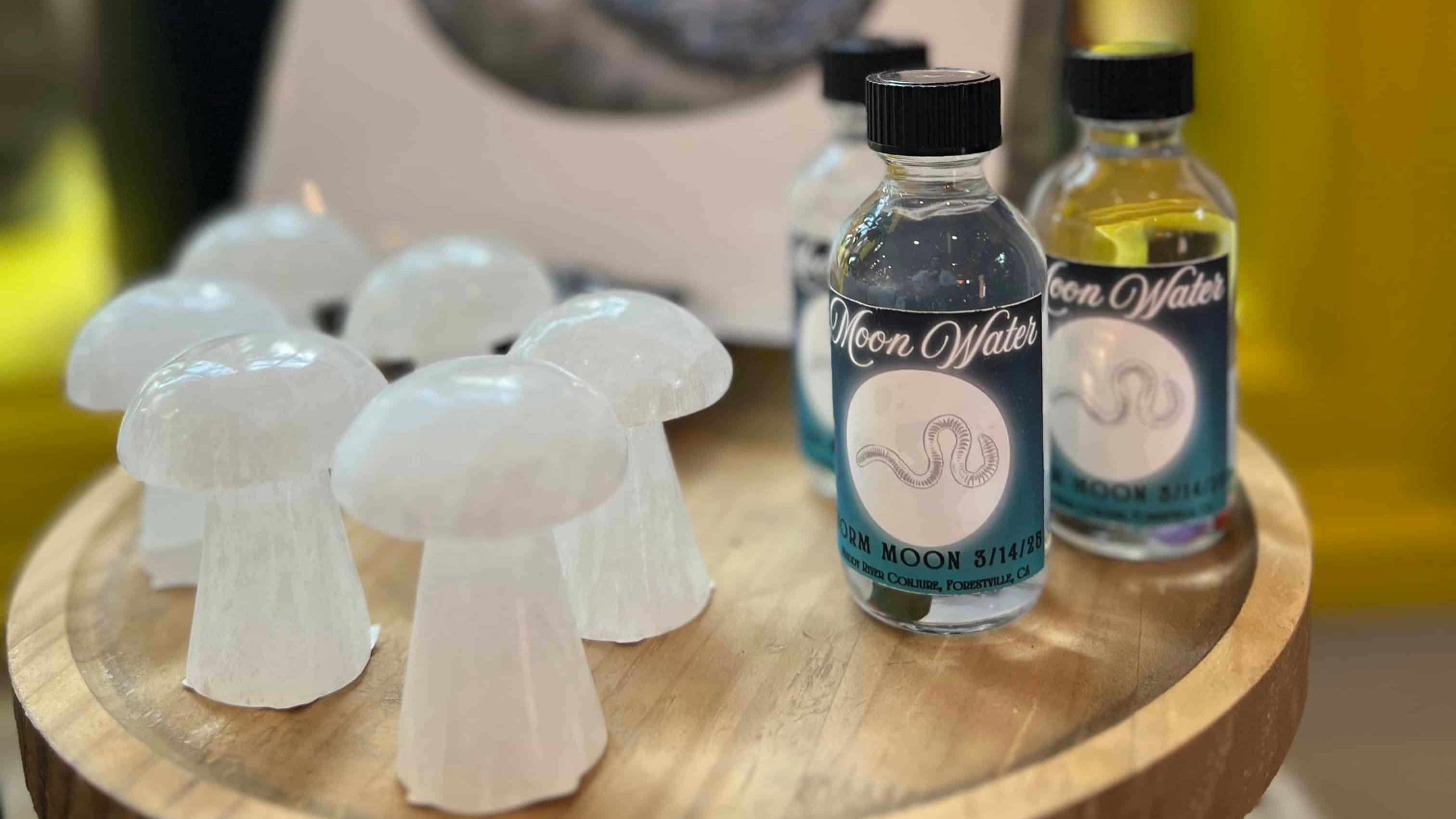 Two bottles of Moon Water on a wooden table with white mushroom-shaped containers.