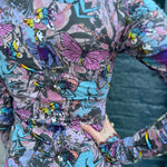 Side detail of printed top with rainbow birds, magic creatures, and soft lettuce hem