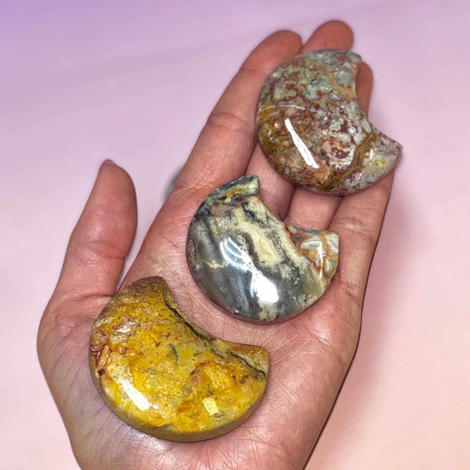 Three polished stones held in a hand against a pink background