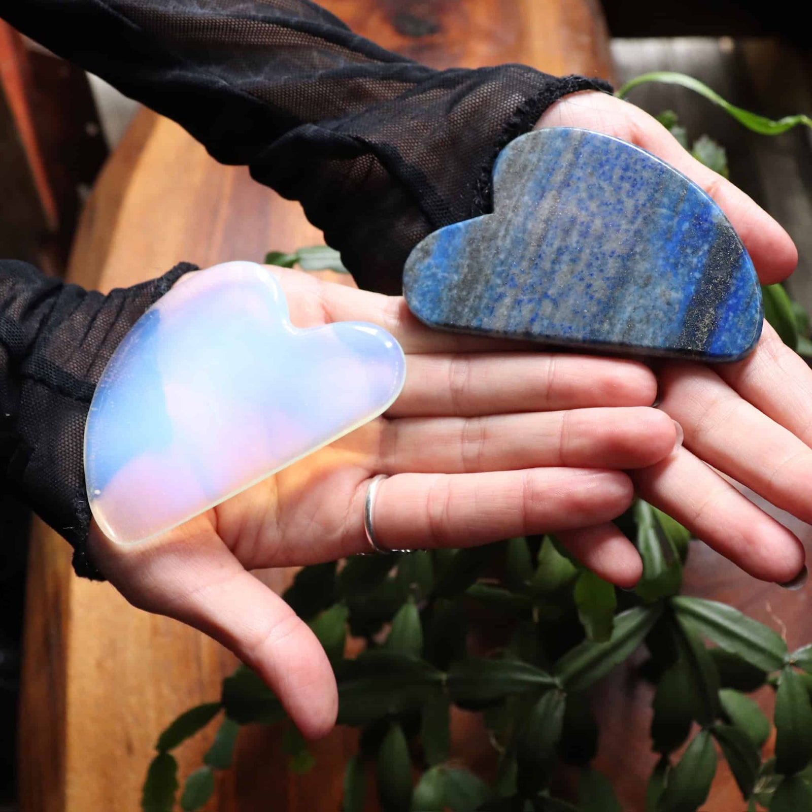 Two hands holding a heart-shaped, multicolored stone and a blue stone.