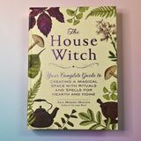 "The House Witch" book on a pink and blue background, showing off the front cover.