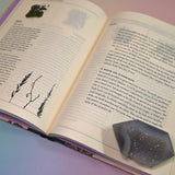 "The Green Witch's Garden" book on a pink and blue background, open and showing some of its pages.