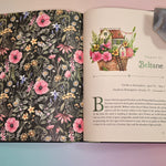 The Witch's Apothecary: Seasons of the Witch Book open and on a pink and blue background with an agate piece holding the open pages down.