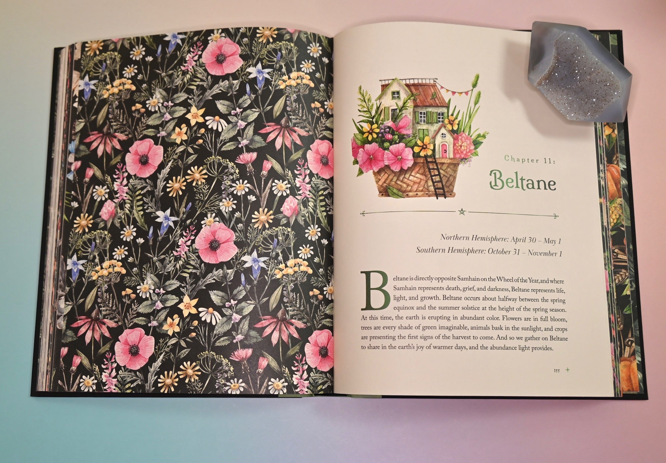 The Witch's Apothecary: Seasons of the Witch Book open and on a pink and blue background with an agate piece holding the open pages down.