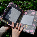 Someone holding the Witch's Apothecary: Seasons of the Witch Book in front of green leaves. The book is open showing some pages.
