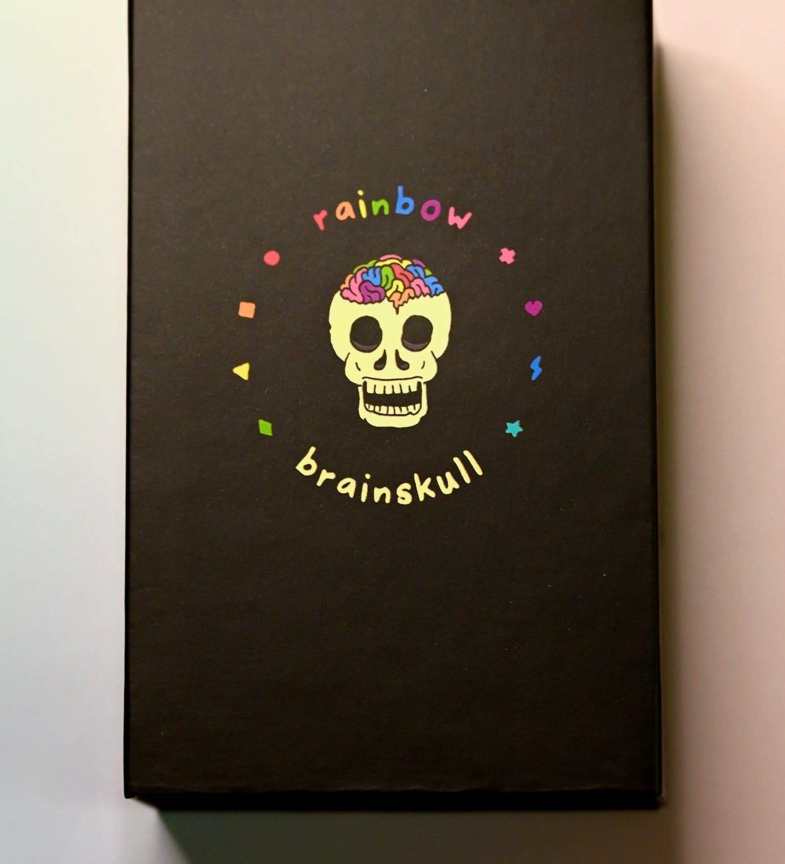 The Rainbow Brainskull Oracle Deck on a pink and blue background.