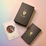 The Rainbow Brainskull Oracle Deck on a pink and blue background with its guidebook and a card next to it.