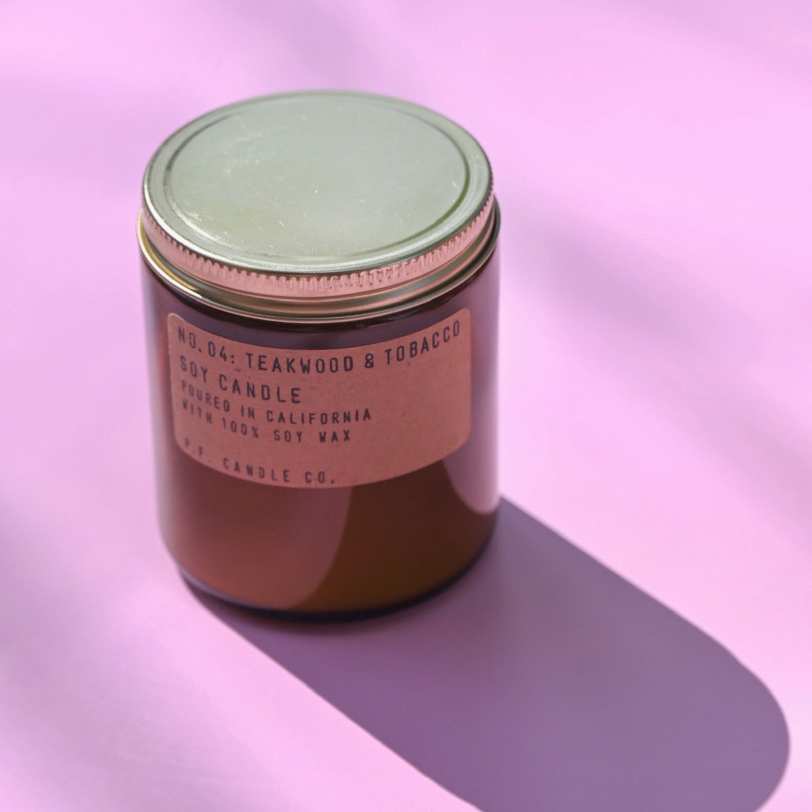 The P.F. Candle Co Teakwood & Tobacco - Standard Soy Candle on a pink background.