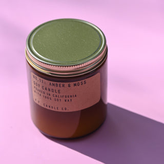 The P.F. Candle Co. - Amber & Moss - 7.2 oz Standard Soy Candle on a pink background.