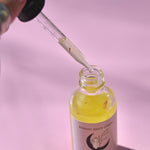 The Healer Potion Body Oil - Lavender Rose Body Oil on a pink background with someone holding the dropper next to the bottle.