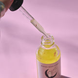 The Healer Potion Body Oil - Lavender Rose Body Oil on a pink background with someone holding the dropper next to the bottle.