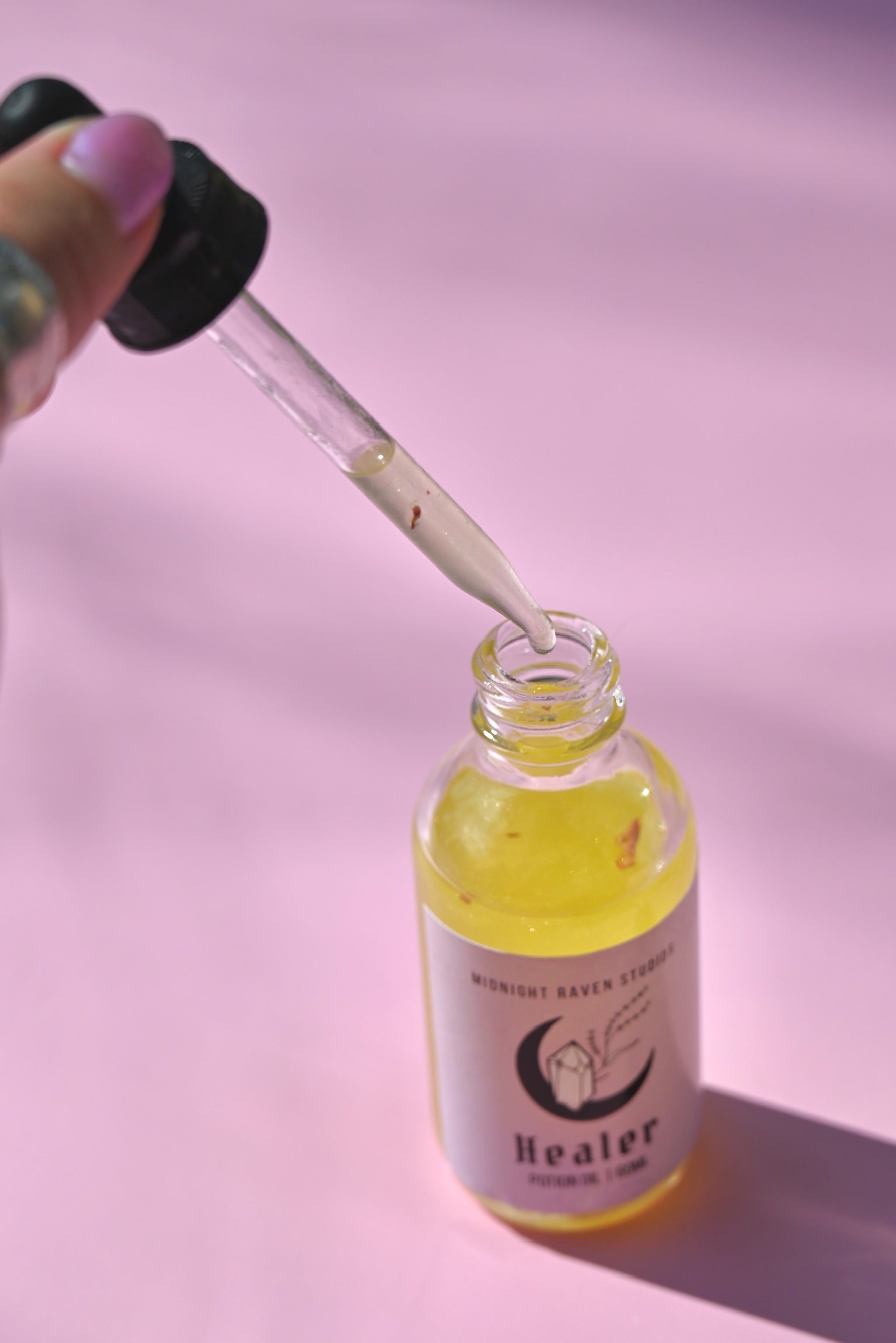 The Healer Potion Body Oil - Lavender Rose Body Oil on a pink background with someone holding the dropper next to the bottle.