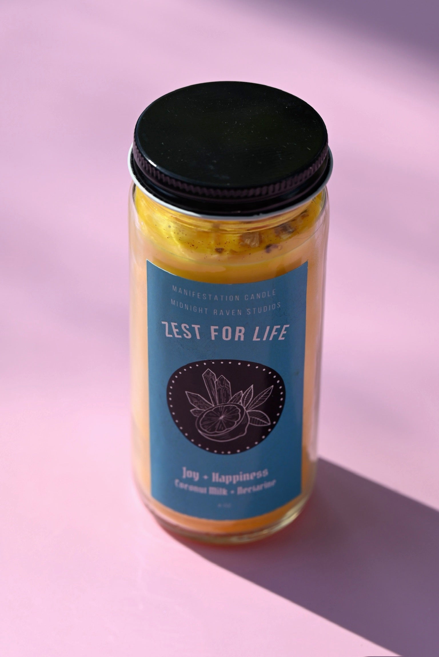 The Zest for Life Spell Candle with Herbs and Crystals on a pink background.