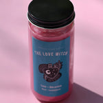 The Love Witch Spell Candle with Herbs and Crystals on a pink background.