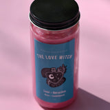 The Love Witch Spell Candle with Herbs and Crystals on a pink background.