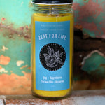 The Zest for Life Spell Candle with Herbs and Crystals in front of a teal background and on a white rusty surface.