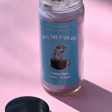 The Chill the F*ck Out Spell Candle with Herbs and Crystals on a pink background with its lid off and to the side.