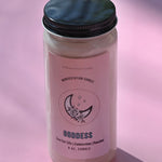 The Goddess Manifestation Candle with Herbs and Crystals on a pink background.
