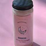 The Goddess Manifestation Candle with Herbs and Crystals on a pink background.