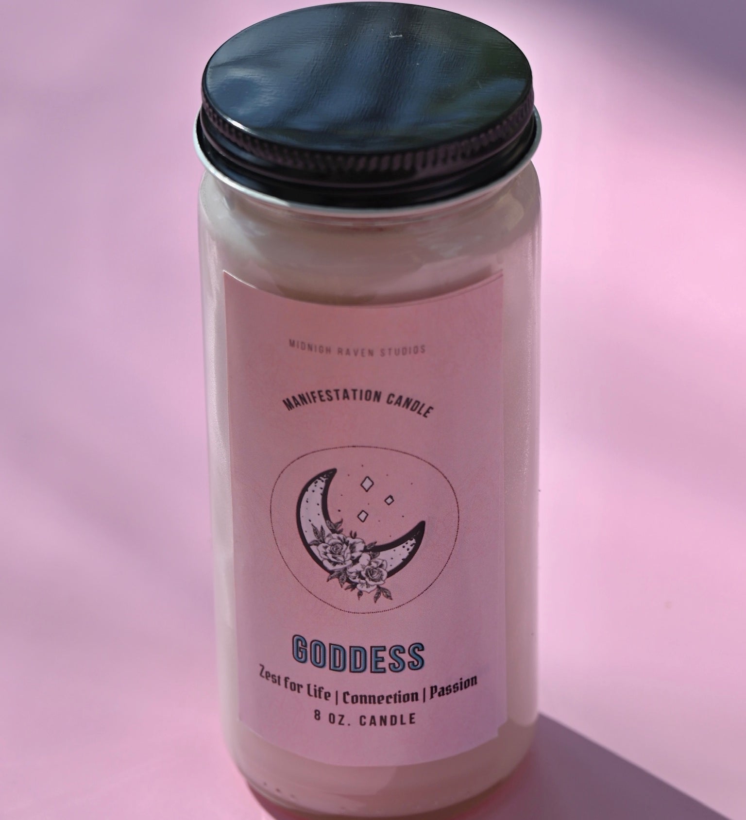 The Goddess Manifestation Candle with Herbs and Crystals on a pink background.
