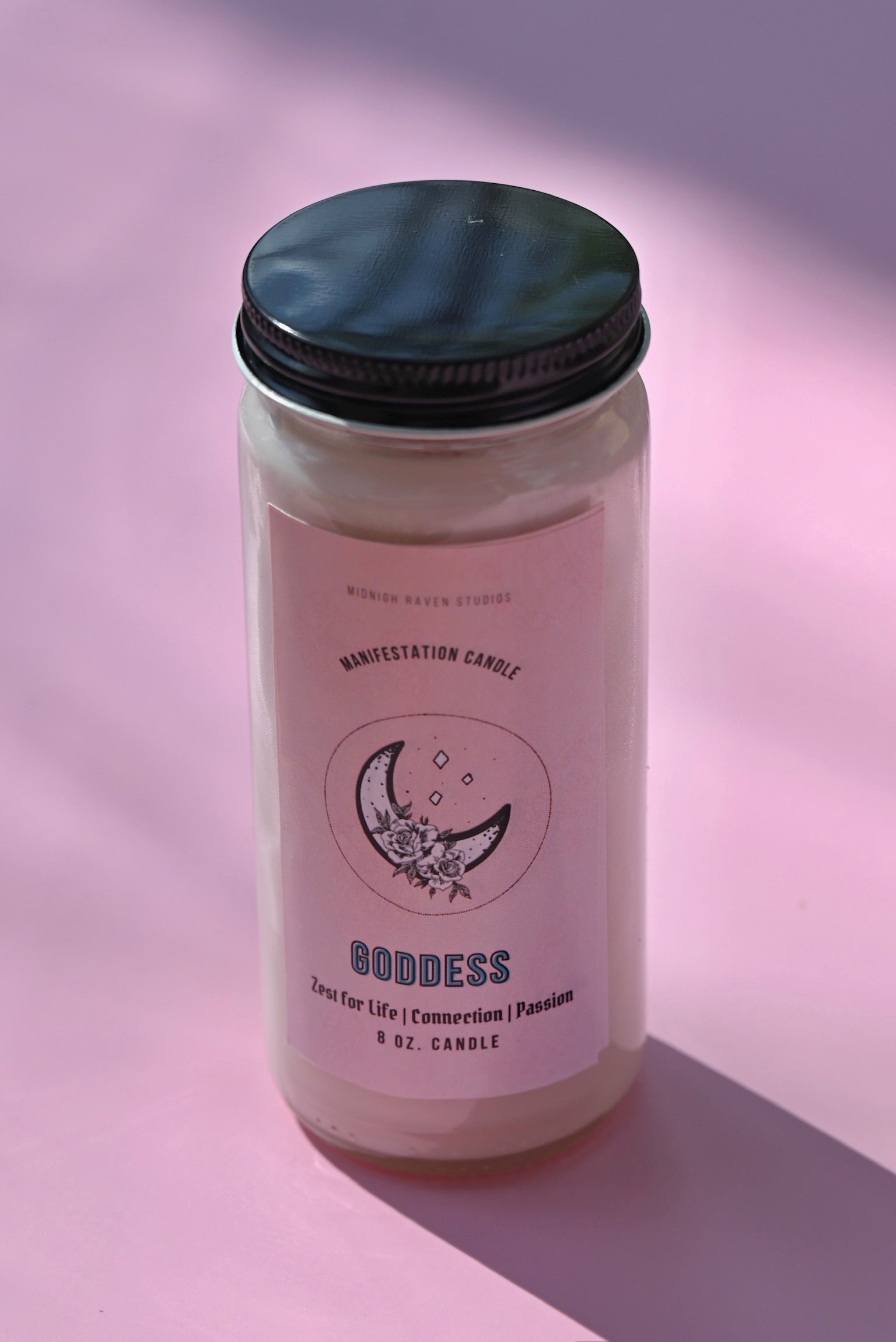 The Goddess Manifestation Candle with Herbs and Crystals on a pink background.