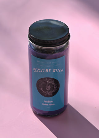 The Intuitive Witch Spell Candle with Herbs and Crystals on a pink background.