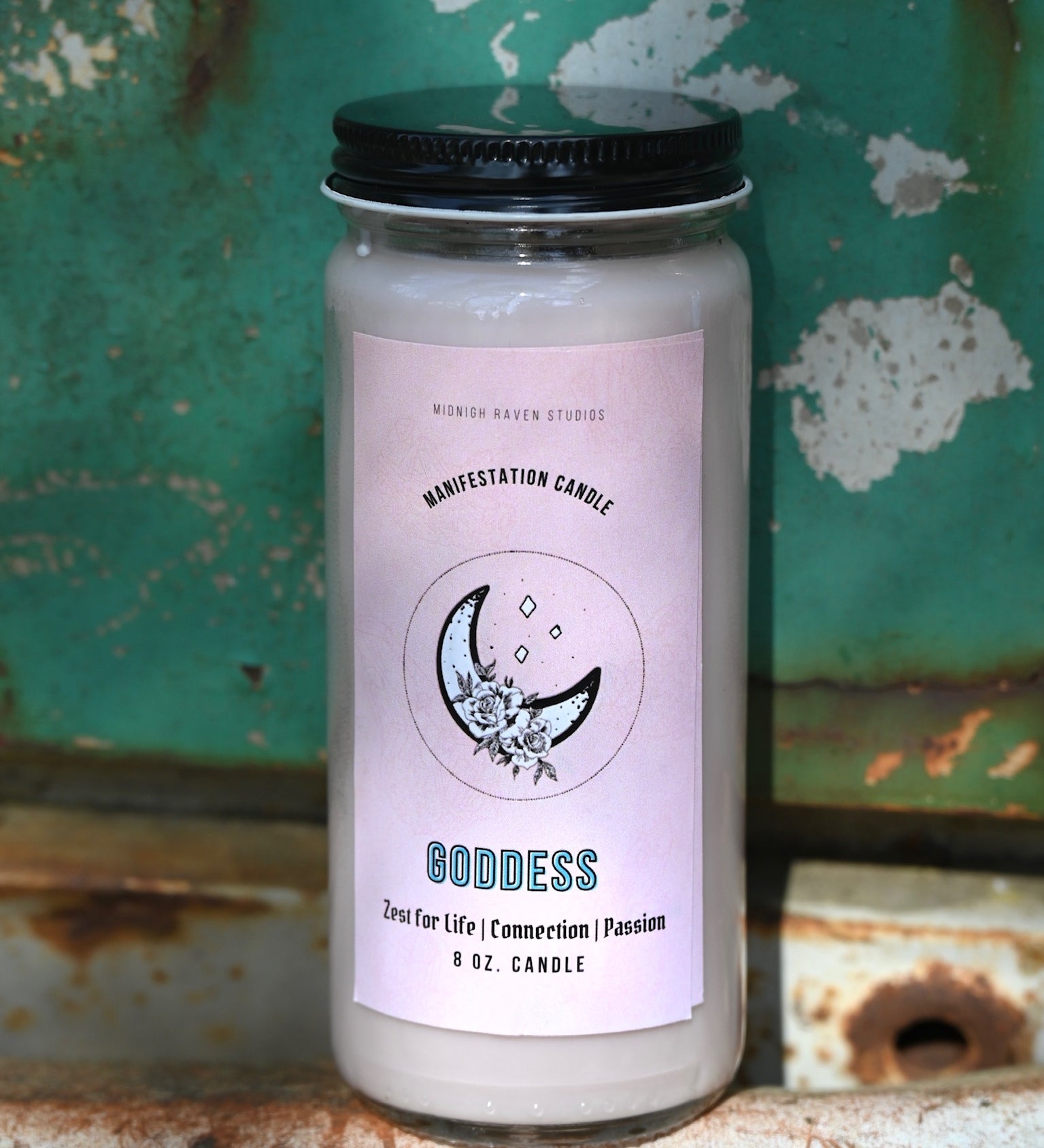 The Goddess Manifestation Candle with Herbs and Crystals in front of a teal background and on a white rusty surface.