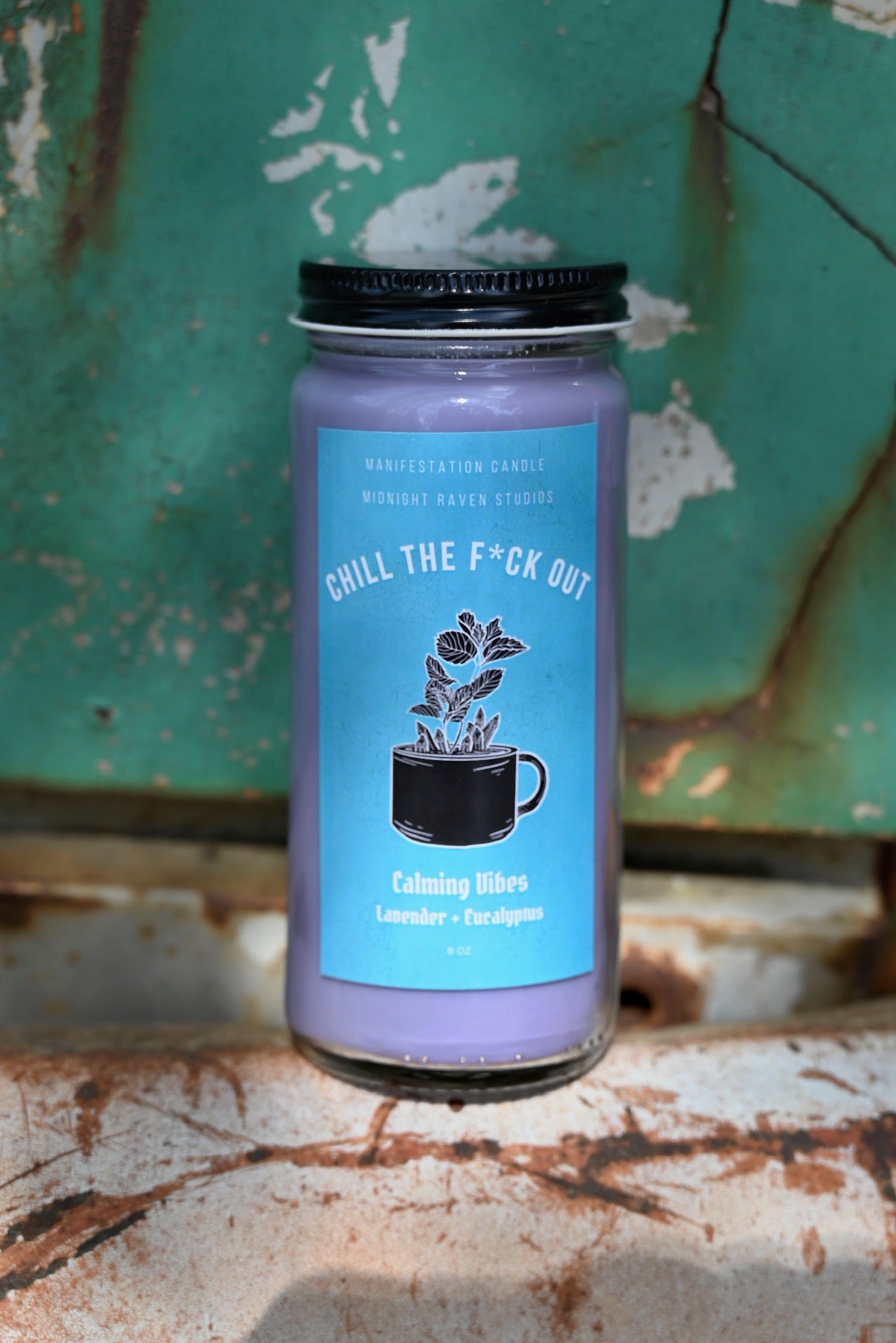 The Chill the F*ck Out Spell Candle with Herbs and Crystals in front of a teal background and on a white rusty surface.