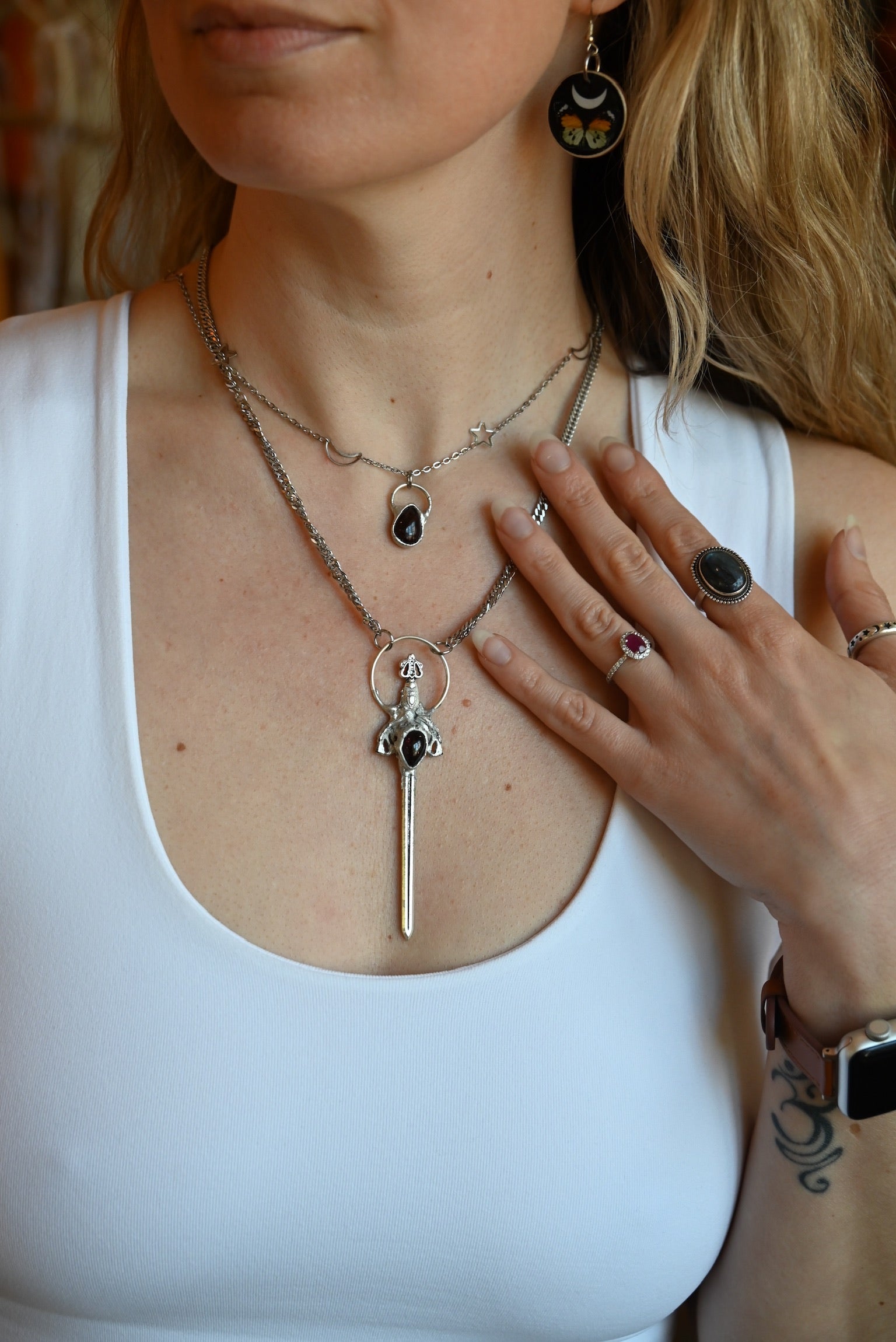 Someone wearing the Sterling Silver Garnet Sword Necklace and the Garnet Sterling Silver Celestial Necklace.