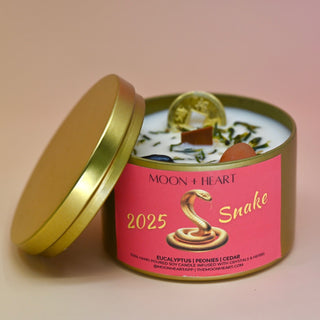 The Year of the Snake Intention & Manifestation Candle - Chinese Zodiac Candle on a pink background with the lid off leaning against the container.