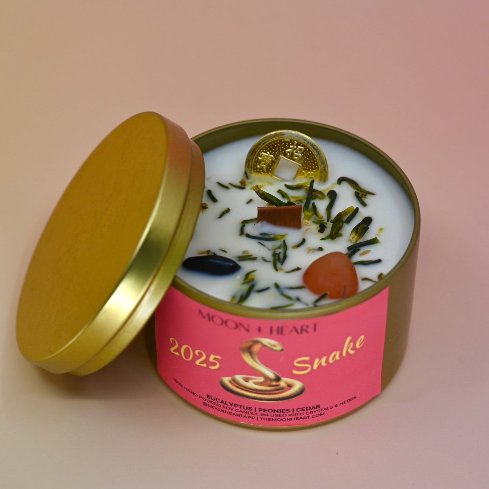 The Year of the Snake Intention & Manifestation Candle - Chinese Zodiac Candle on a pink background with the lid off leaning against the container.