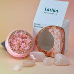 The Rose Quartz Crystal Bath Bomb out of its box surrounded by rose quartz pieces on a pink background.