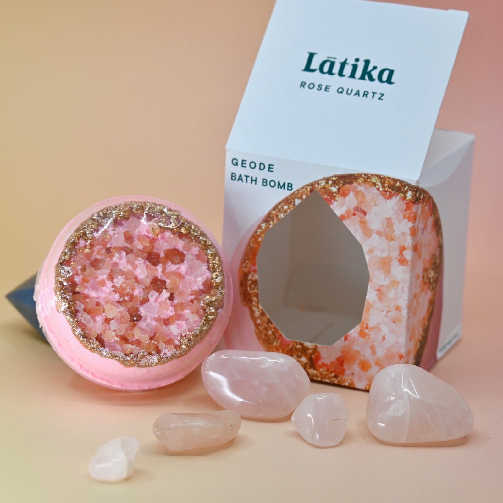 The Rose Quartz Crystal Bath Bomb out of its box surrounded by rose quartz pieces on a pink background.