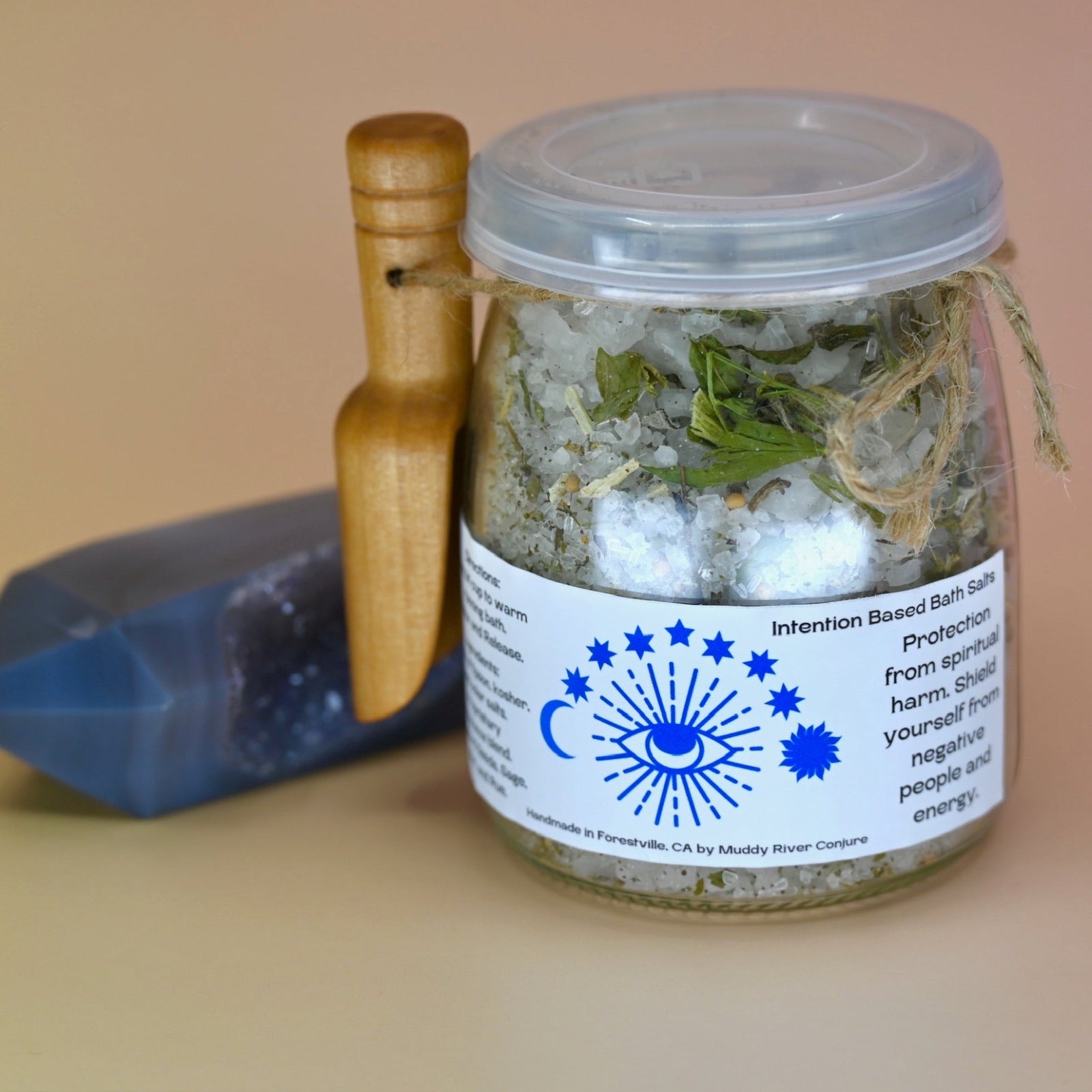 The Spiritual Protection Bath Crystal Salts on a pink background with an agate crystal piece to its left.