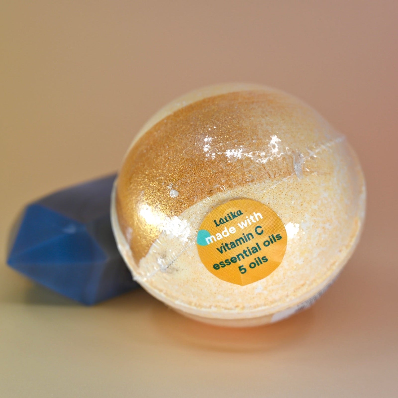The Orange Essential Oil Vitamin C Bath Bomb on a dusty pink background next to a crystal piece.