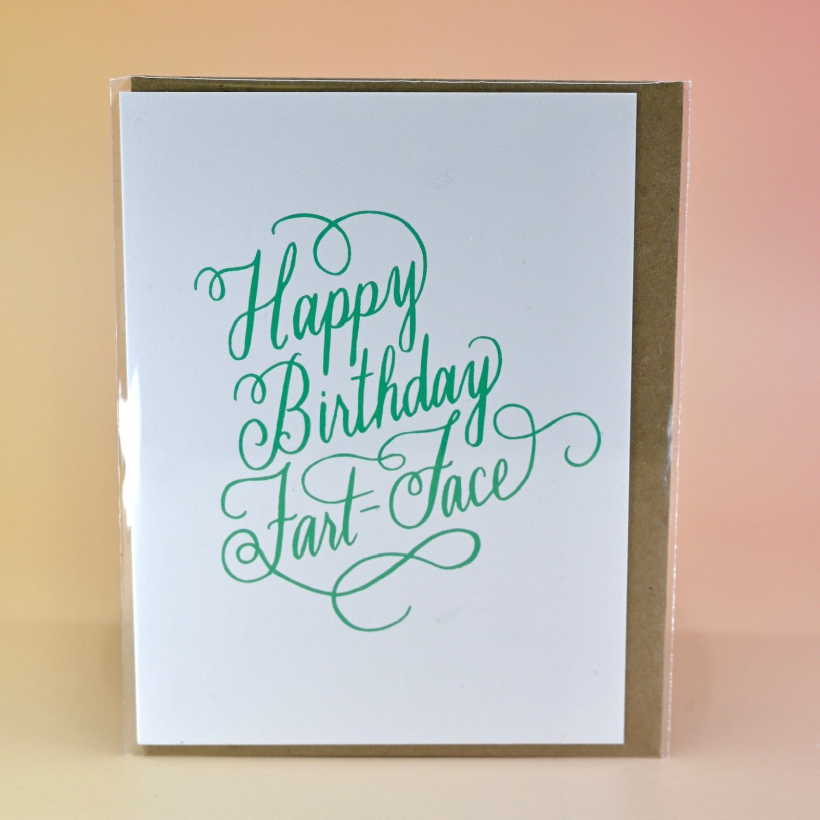 The Happy Birthday Fart Face Greeting Card on a peach-colored background.