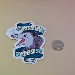 The Internally Screaming Possum Sticker next to a quarter on a tan background.
