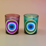 The Green and Purple Evil Eye Votive Candles on a peach-colored background.