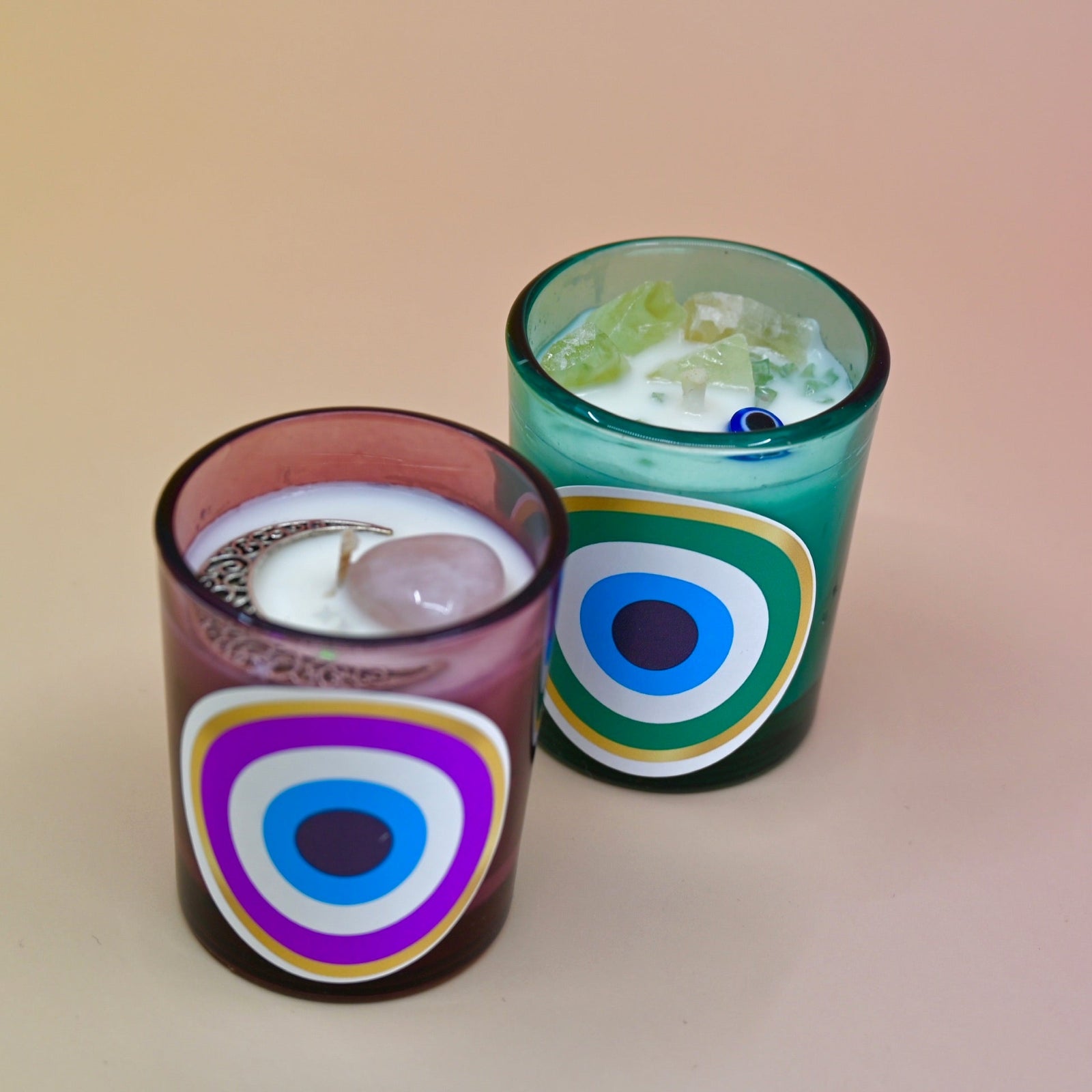 The Green and Purple Evil Eye Votive Candles on a peach-colored background.