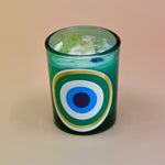 The Green Evil Eye Votive Candle on a peach-colored background.