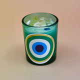 The Green Evil Eye Votive Candle on a peach-colored background.