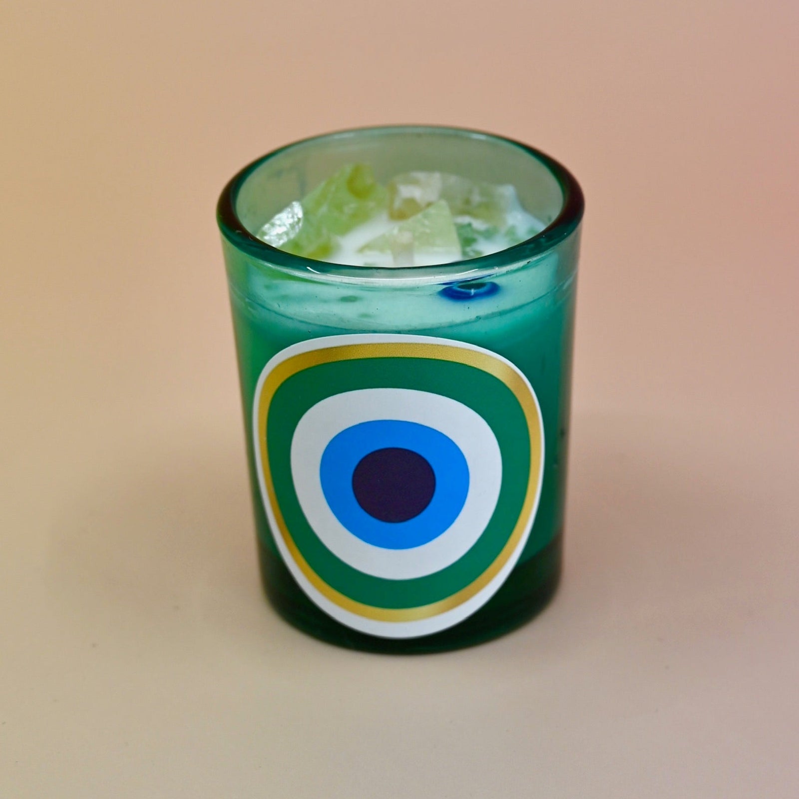 The Green Evil Eye Votive Candle on a peach-colored background.