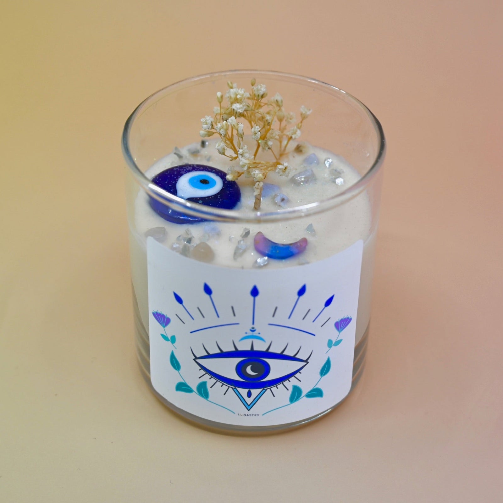 The Evil Eye Soy Wax Candle on a peach-colored background.