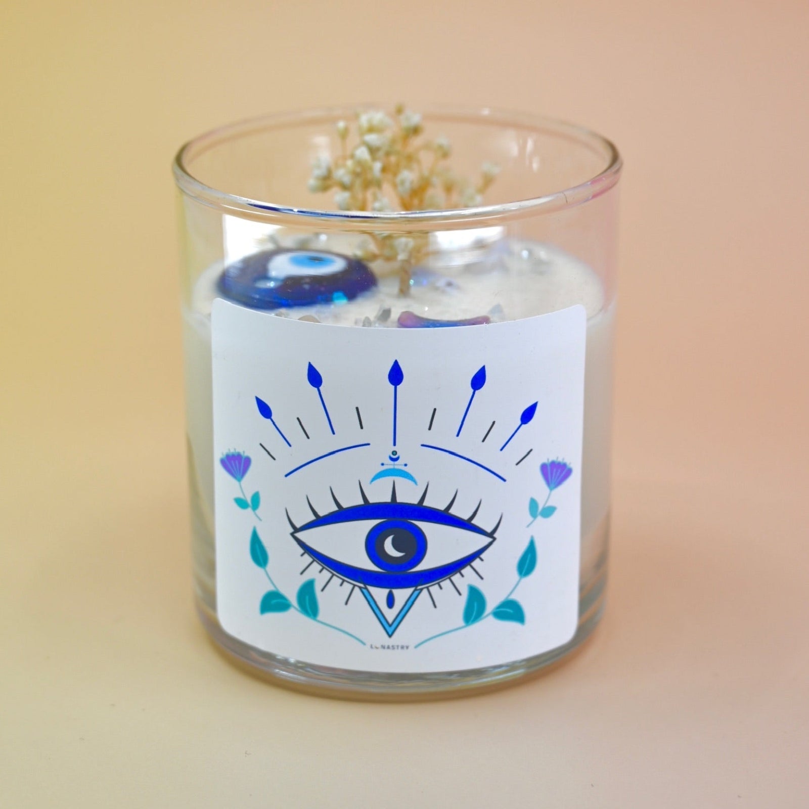 The Evil Eye Soy Wax Candle on a peach-colored background.