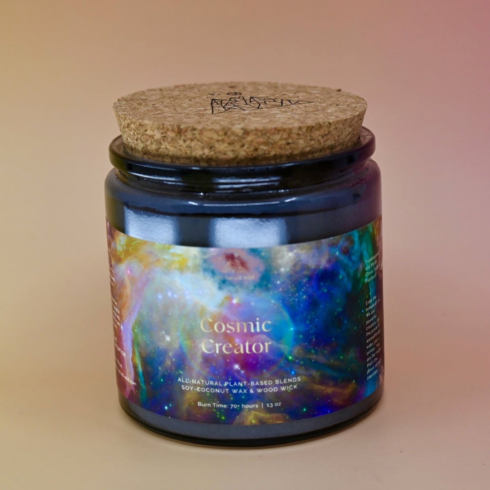 The Cosmic Creator Intention Candle on a a pink and yellow background with the cork lid on.