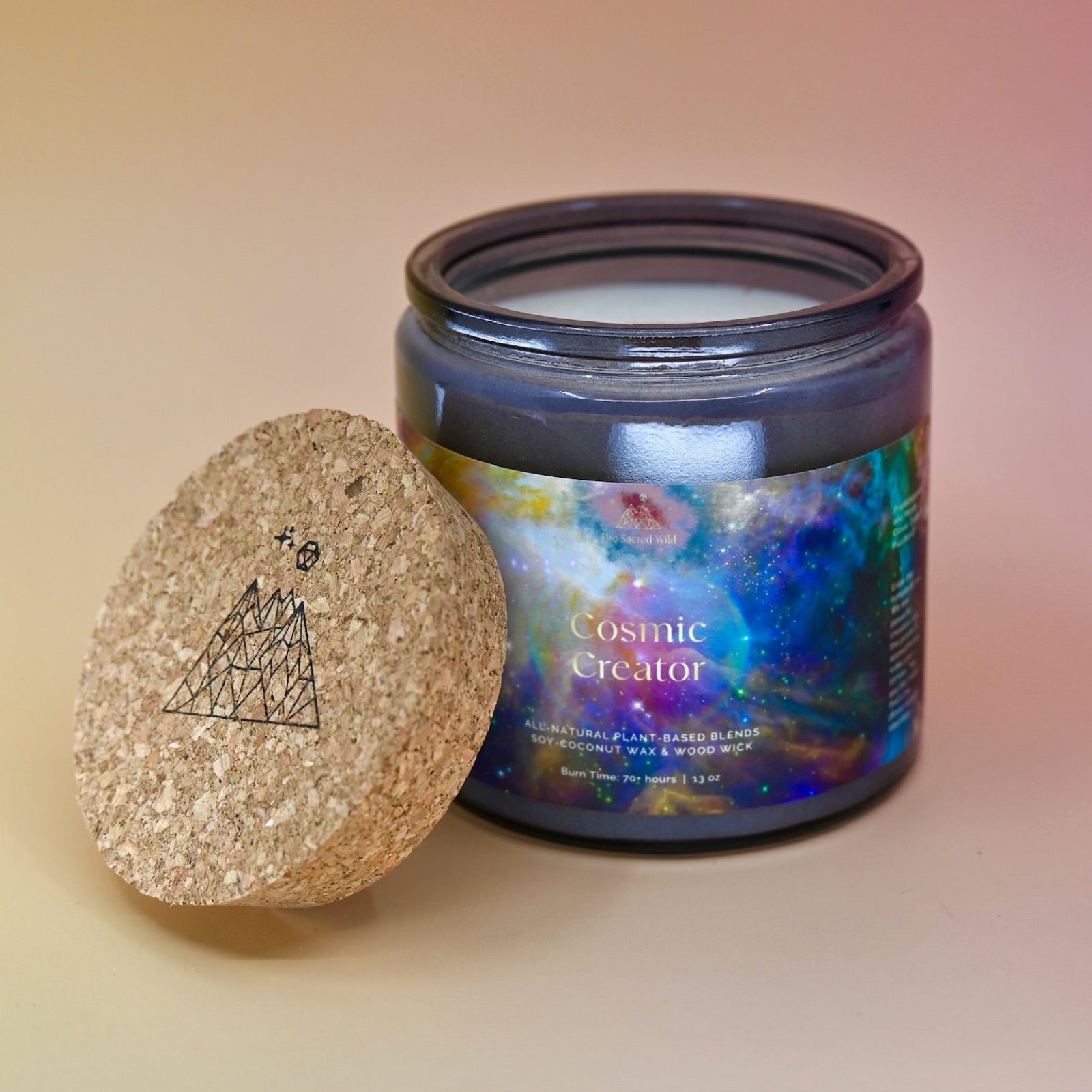 The Cosmic Creator Intention Candle on a a pink and yellow background with the lid off leaning against the candle jar.