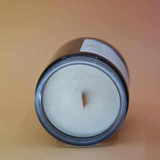 The Moons Ritual Candle on a pink and yellow background lying on its side showing off the wooden wick and gray sparkles in the candle.